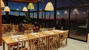 Ambiente interno do Restaurante OKRA, com decoração contemporânea, mesas de madeira e vista para as montanhas da serra mineira.